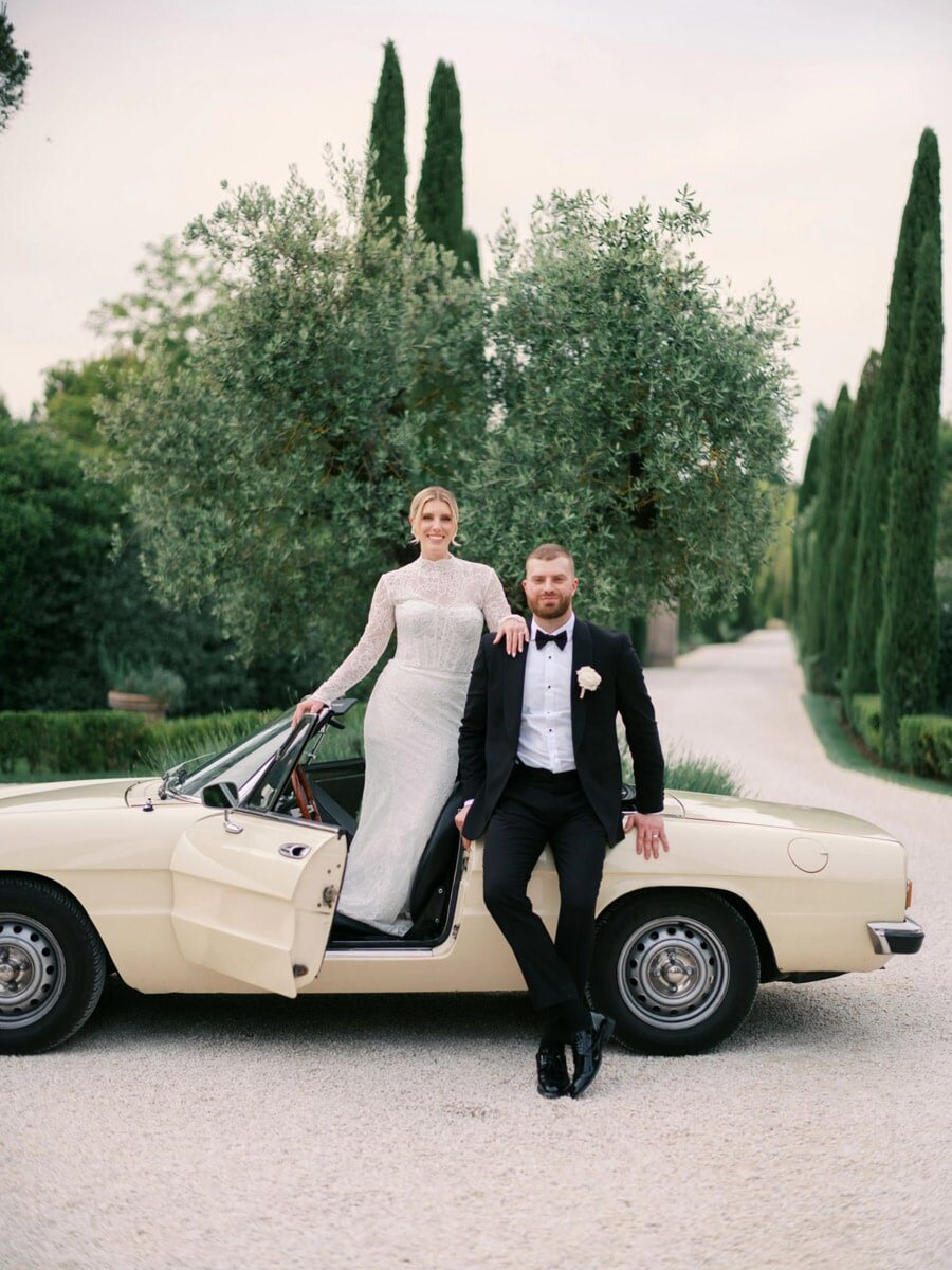 Couple in front of antic Alpha Romeo during their Borgo Santo Pietro wedding in Tuscany. By international photographer Andreas K. Georgiou