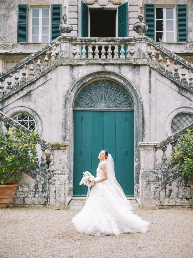 A bride stands gracefully in front of villa Cetinal. She wears a flowing white gown and veil, holding a bouquet.